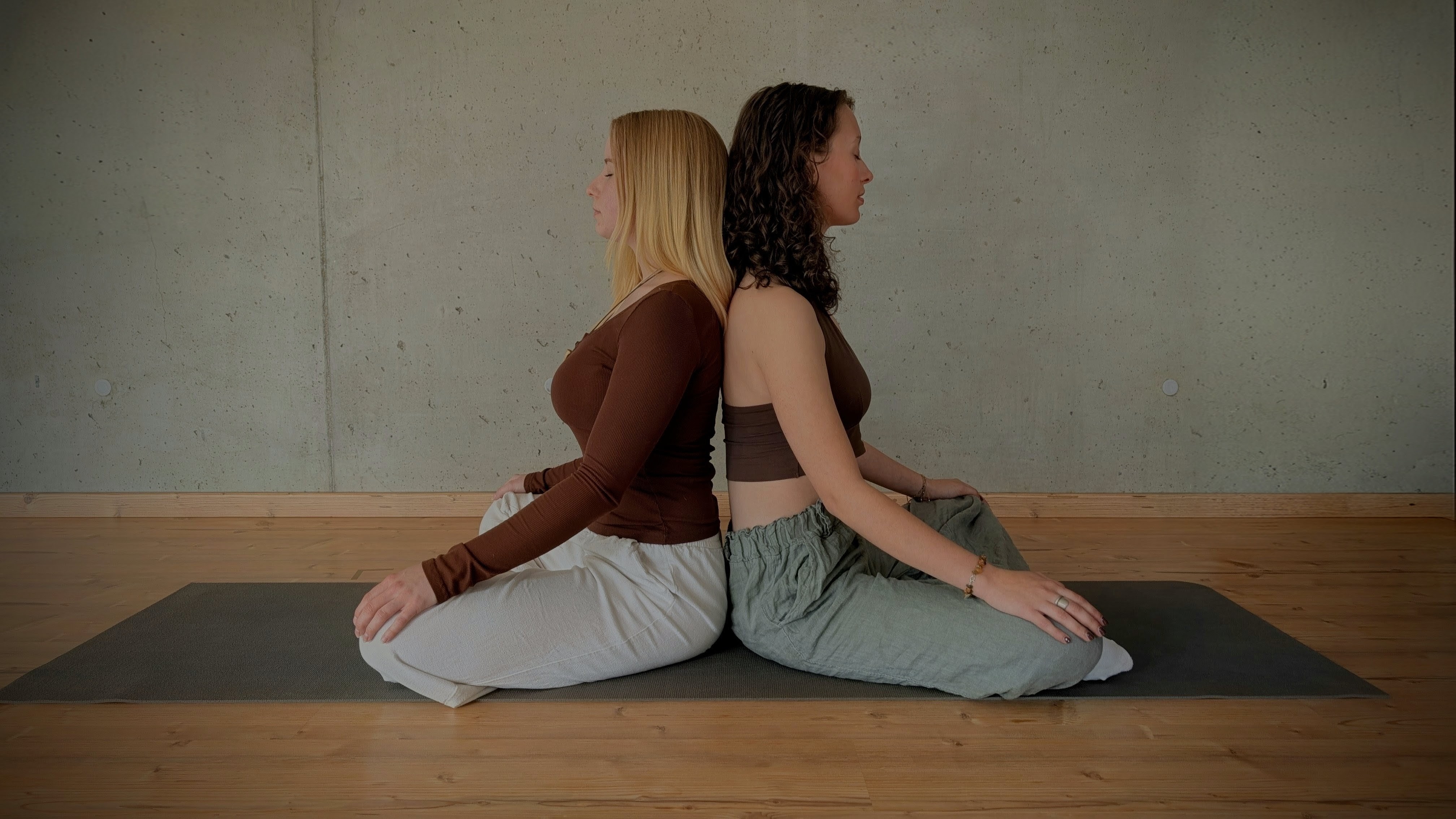 Two women sitting back to back in meditation